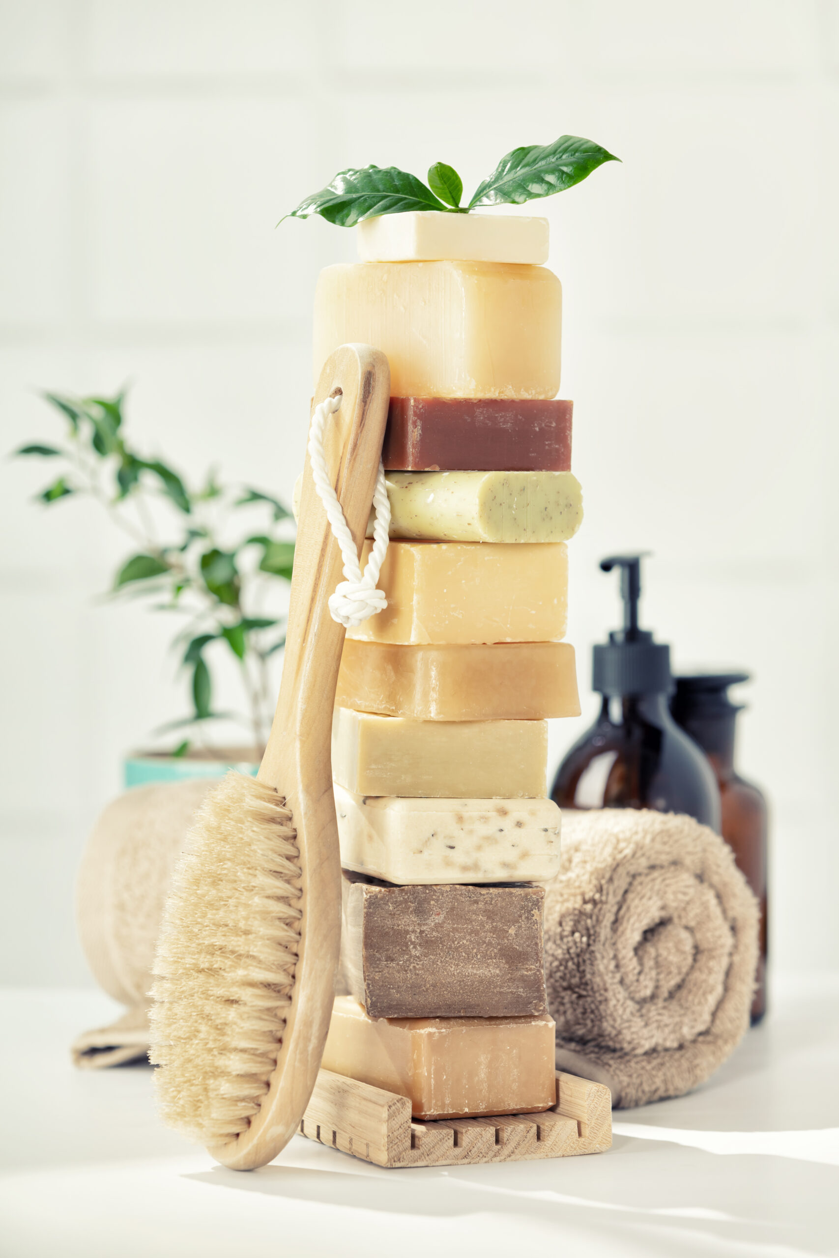 Variety of natural organic handmade soap bars on white bathroom countertop, wooden massage brush, towel and scincare accessories