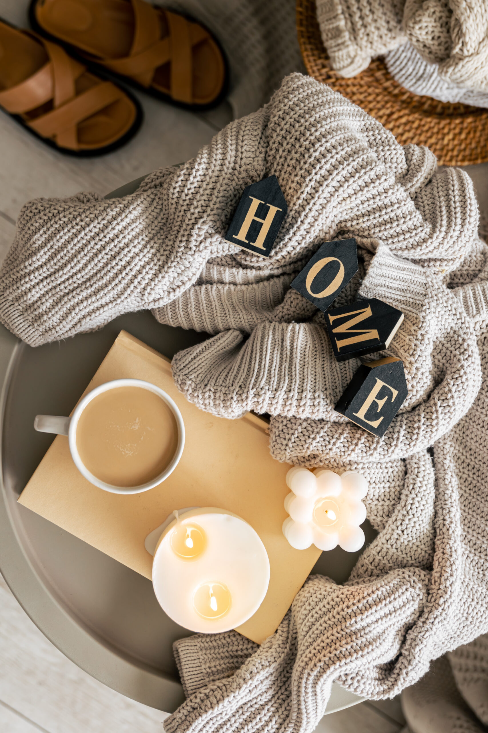 Cozy composition with decorative word home, knitted element, candles and a cup of coffee.